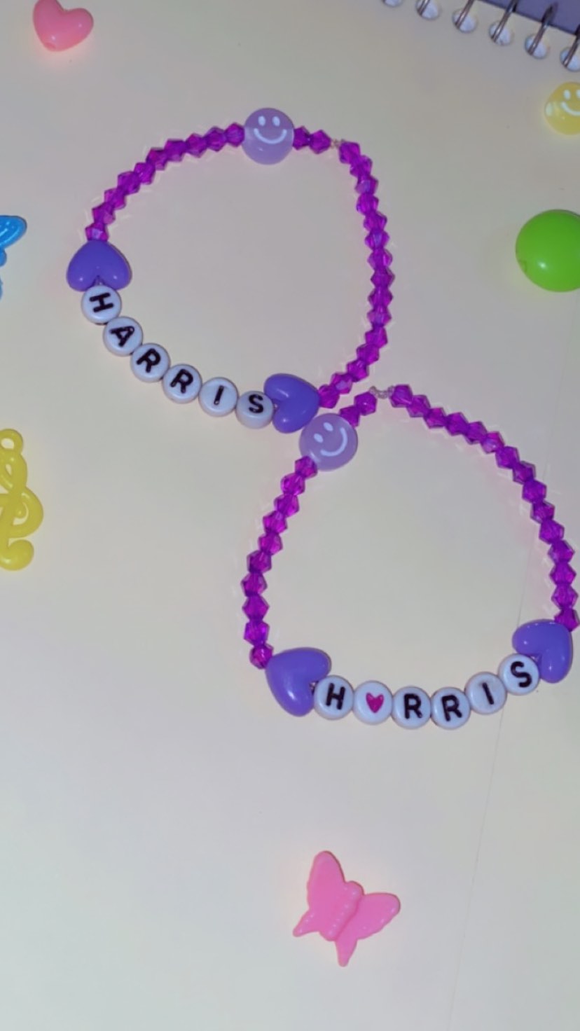 Close-up of two purple beaded bracelets spelling ‘HARRIS’, surrounded by colorful hearts and a butterfly beed on a light background.